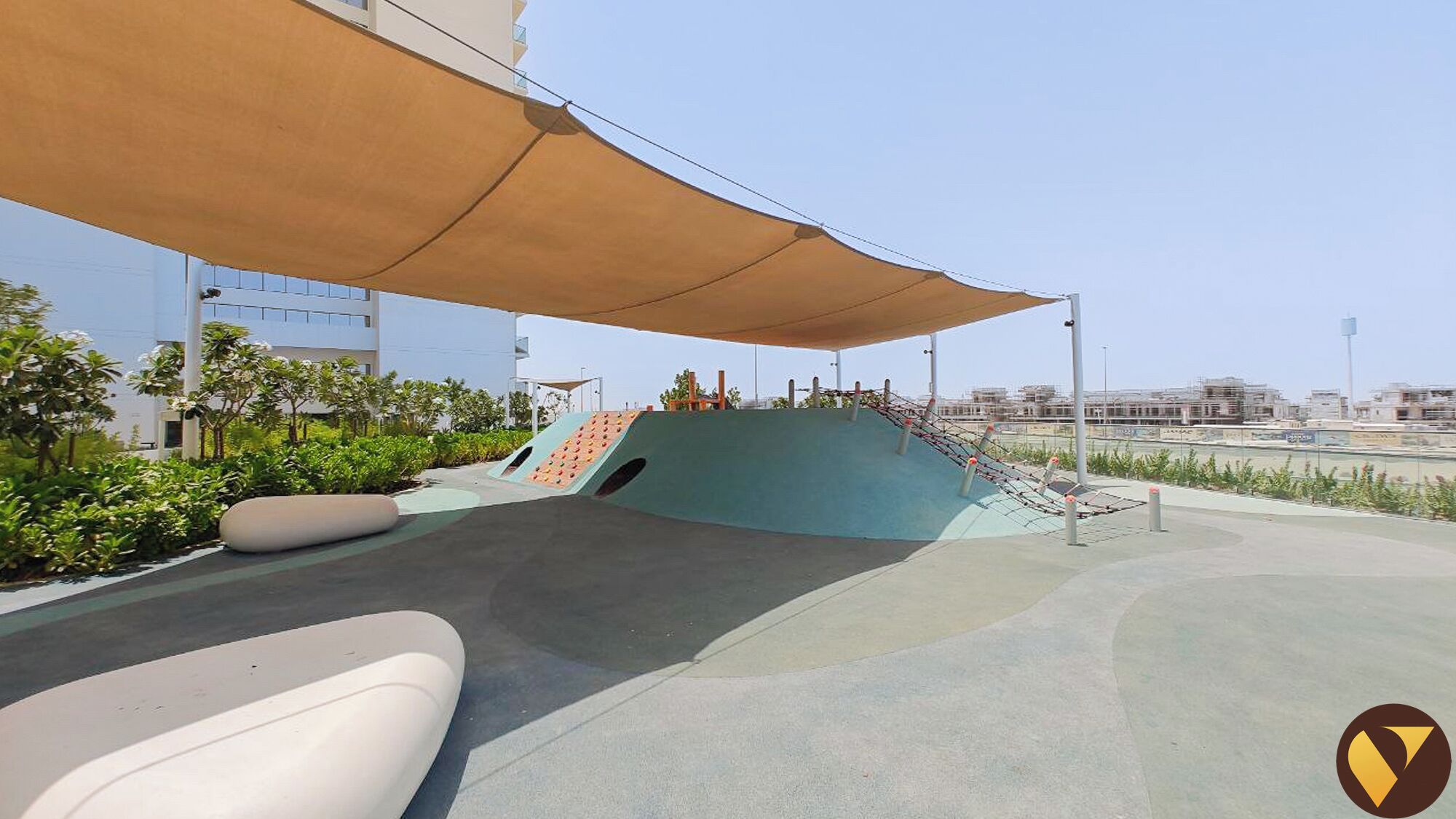 A rooftop playground with a slide and climbing wall, surrounded by greenery and a large canopy.
