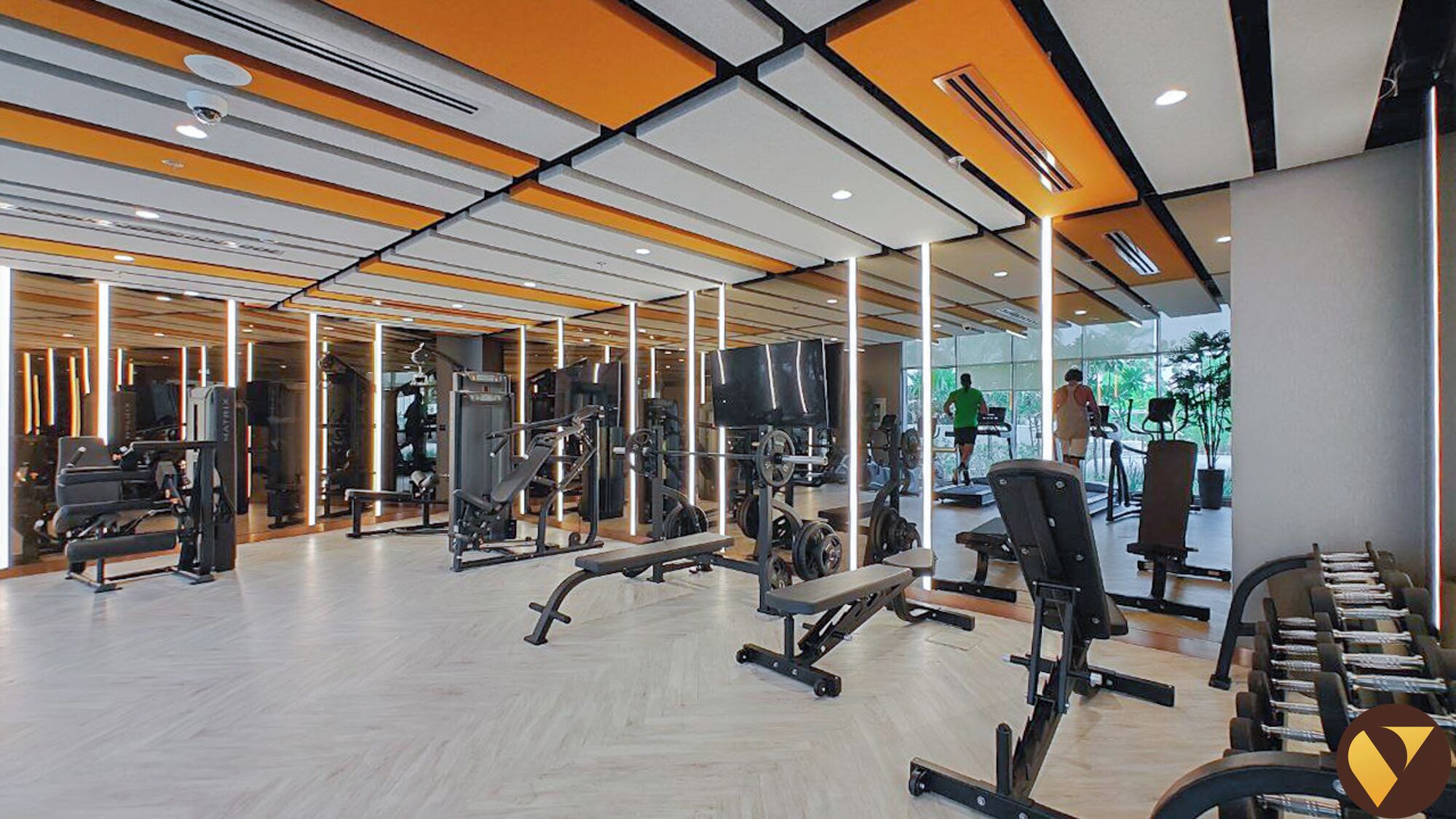 A modern gym with various exercise equipment, large windows, and a wooden floor.
