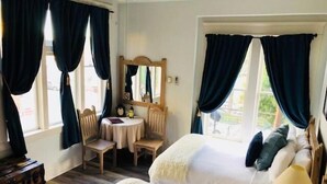 A room with two beds, a small table with chairs, a mirror, and a wooden chest of drawers. - Hotel San Ramon (Bisbee)