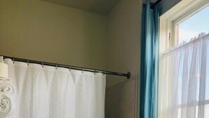 A bathroom with a white toilet, a shower curtain, and a window with blue curtains. - Hotel San Ramon (Bisbee)