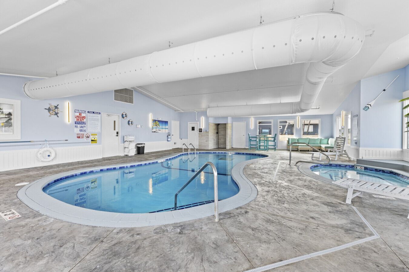 An indoor swimming pool with multiple lanes, a lifeguard station, and a lounge area with seating.