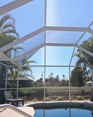 A covered outdoor area with a pool, chairs, and palm trees.