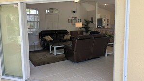 Ein Wohnzimmer mit einer schwarzen Ledersofa, einem Couchtisch und einer Lampe. Eine Tür führt in einen anderen Raum.