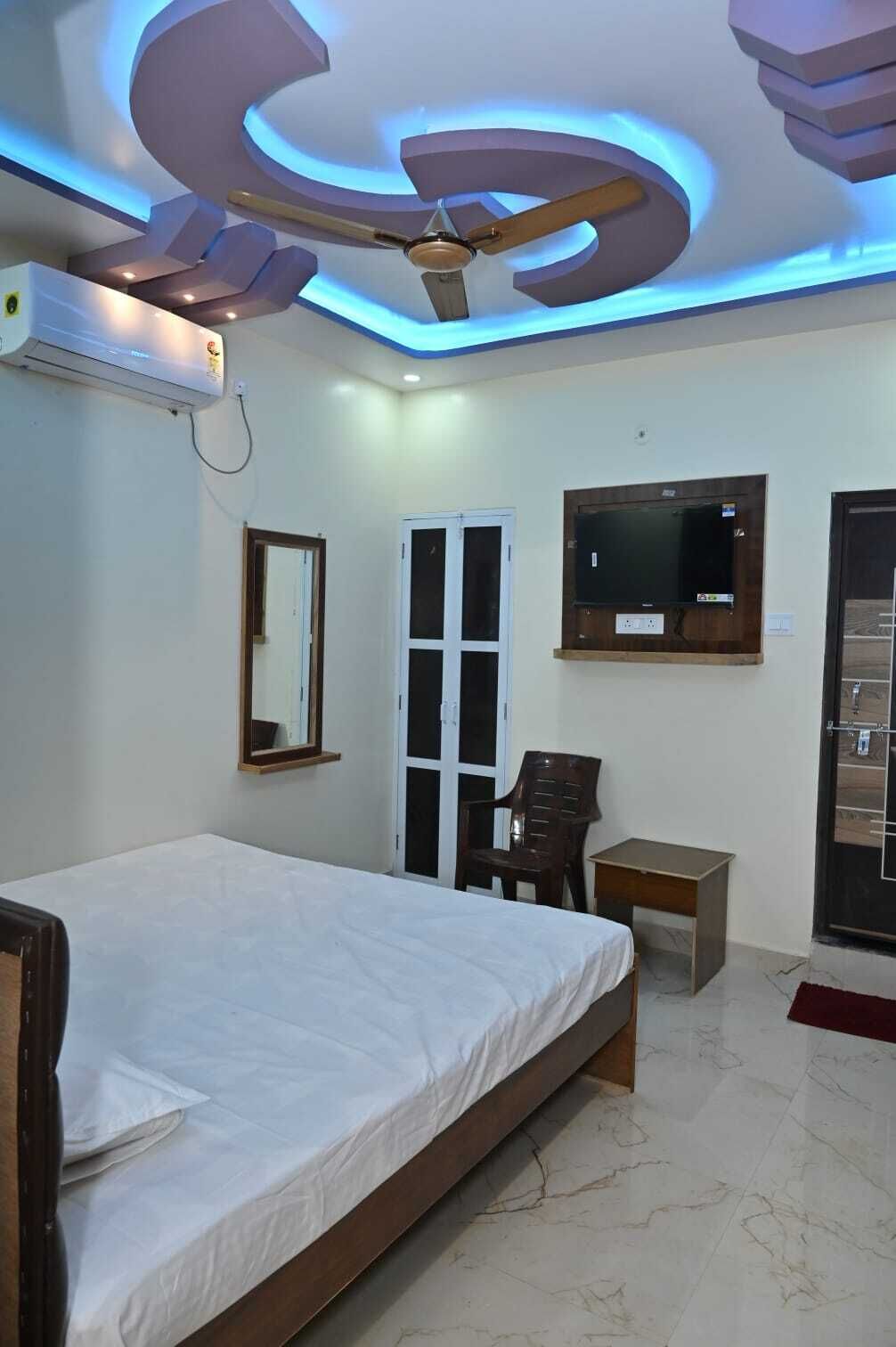 Un dormitorio con cama, ventilador de techo, aire acondicionado, televisor, espejo y puerta.