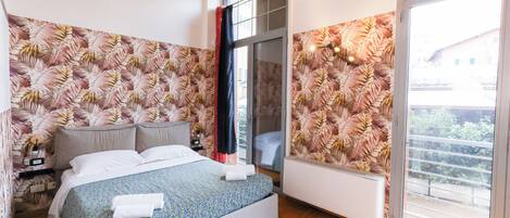 A bedroom with a bed, a nightstand, a window with a view, and a wall with a leaf pattern.