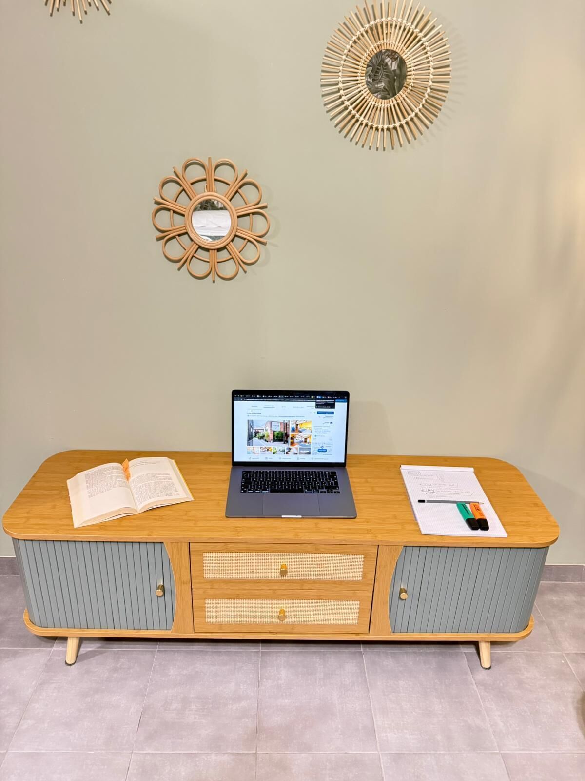 Un escritorio de madera con una computadora portátil, un libro abierto y un bloc de notas con marcadores.