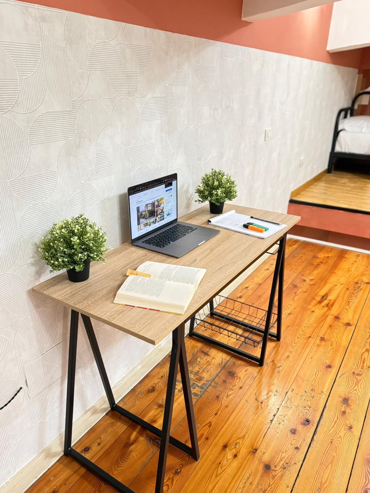 A wooden desk with a laptop, open book, and two small potted plants.