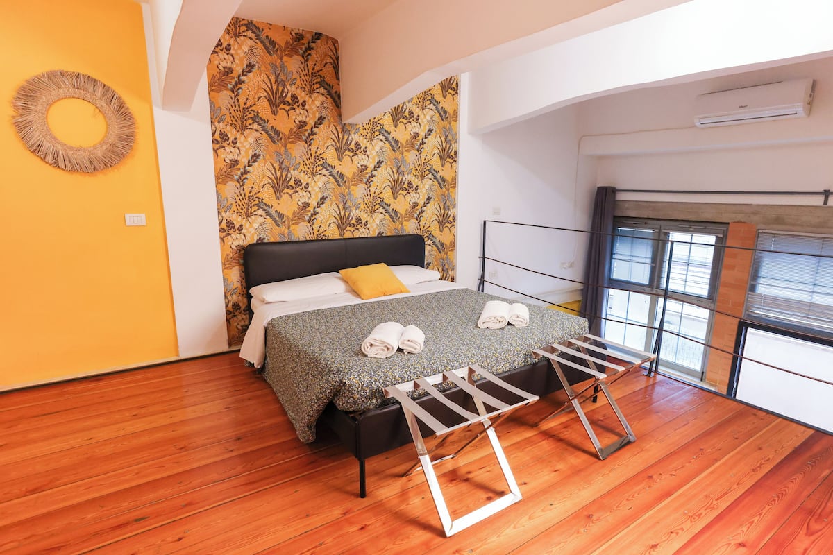 A bedroom with a bed, a wooden floor, a patterned wall, and a window.