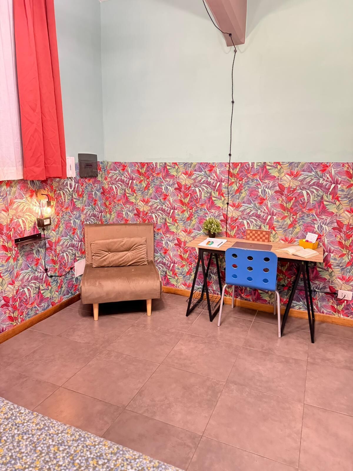 Een kamer met een bruine bank, een klein tafeltje met een plant en kleurrijke bloemenbehang.