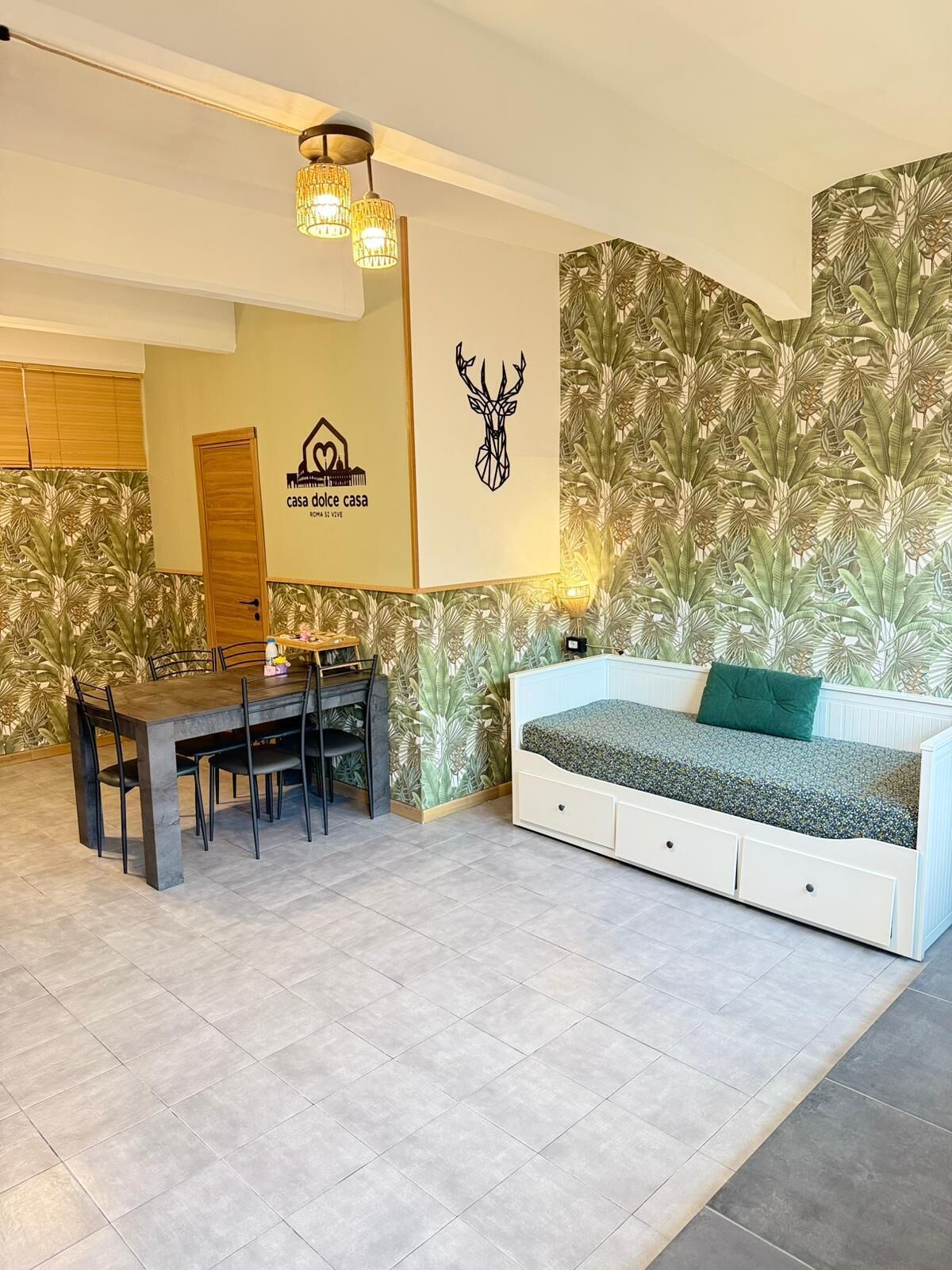 Una habitación con una mesa de comedor, sillas, un sofá y una pared con estampado de hojas tropicales.
