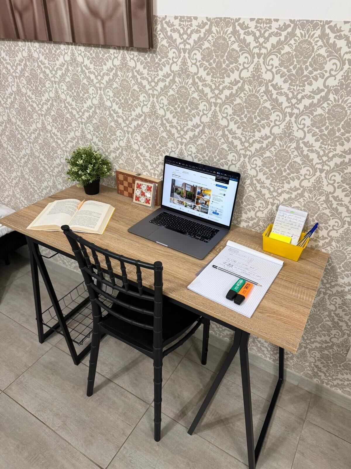 A wooden desk with a laptop, open books, a small potted plant, and a chessboard.