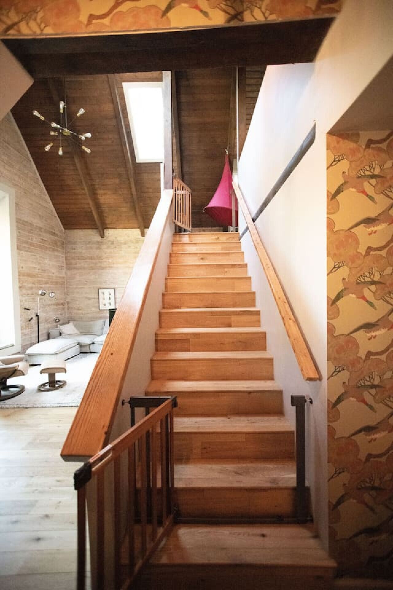 A wooden staircase with a red canopy, leading to a room with a modern design and a patterned wall.