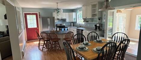 A spacious kitchen with wooden flooring, white cabinets, and a dining area with a wooden table and chairs.