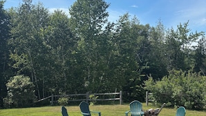 Un patio con sillas Adirondack y un brasero, rodeado de césped y árboles.