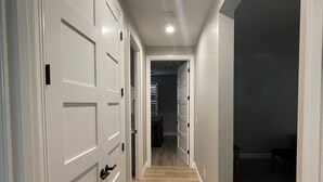 Un pasillo con puertas blancas, piso de madera y una lámpara en el techo.