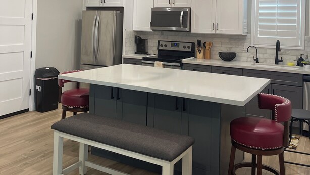 Una cocina moderna con armarios blancos, electrodomésticos de acero inoxidable, una isla central con asientos y un ventilador de techo.