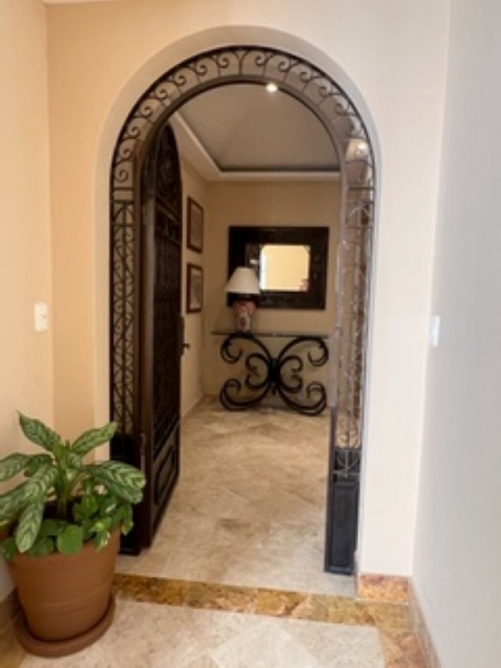 A hallway with a decorative archway, a potted plant, and a lamp.