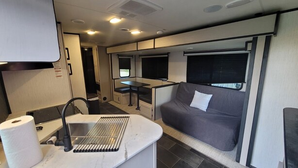 Interior d'una caravana de dimensions compactes amb petita cuina, un bany, una zona de dinar i un sofà.