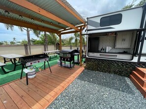 An RV with a kitchen area, a barbecue grill, and a picnic table on a covered deck. - Family and Friends Retreat RV’s Village at Jobos Isabela (Jobos)