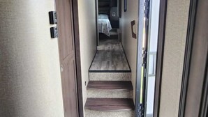 Un passadís estret amb un estriquet blau a l'entrada, uns escalons de fusta que porten a una habitació, i una porta amb un extintor.