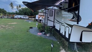 Una caravana amb zona d'estar coberta, envoltada d'un prat i palmeres.