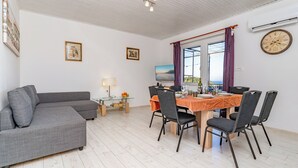 Un salon moderne avec un canapé d’angle gris, une table à manger avec quatre chaises et une grande fenêtre agrémentée de rideaux violets.