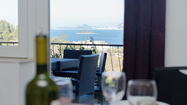 Un coin repas avec vue sur la mer, une bouteille de vin et un verre sur la table.