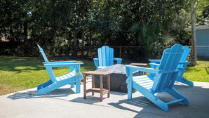 Un patio con sillas Adirondack azules y una pequeña mesa, rodeado de césped y árboles.