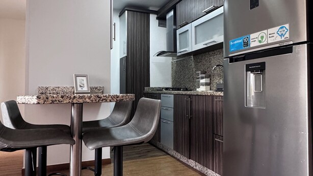 A modern kitchen with a stainless steel refrigerator, a built-in microwave, and a water dispenser. There are two bar stools and a granite countertop.