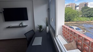 A modern room with a flat-screen TV, a laptop on a dark table, and a potted plant.