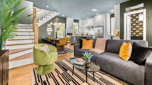 A modern living room with a grey sofa, green armchair, and a staircase leading to a kitchen area. - Designer Spa Retreat Near Historic Downtown! Pets! Luxury Walk to Shops & Dining (St. Augustine)