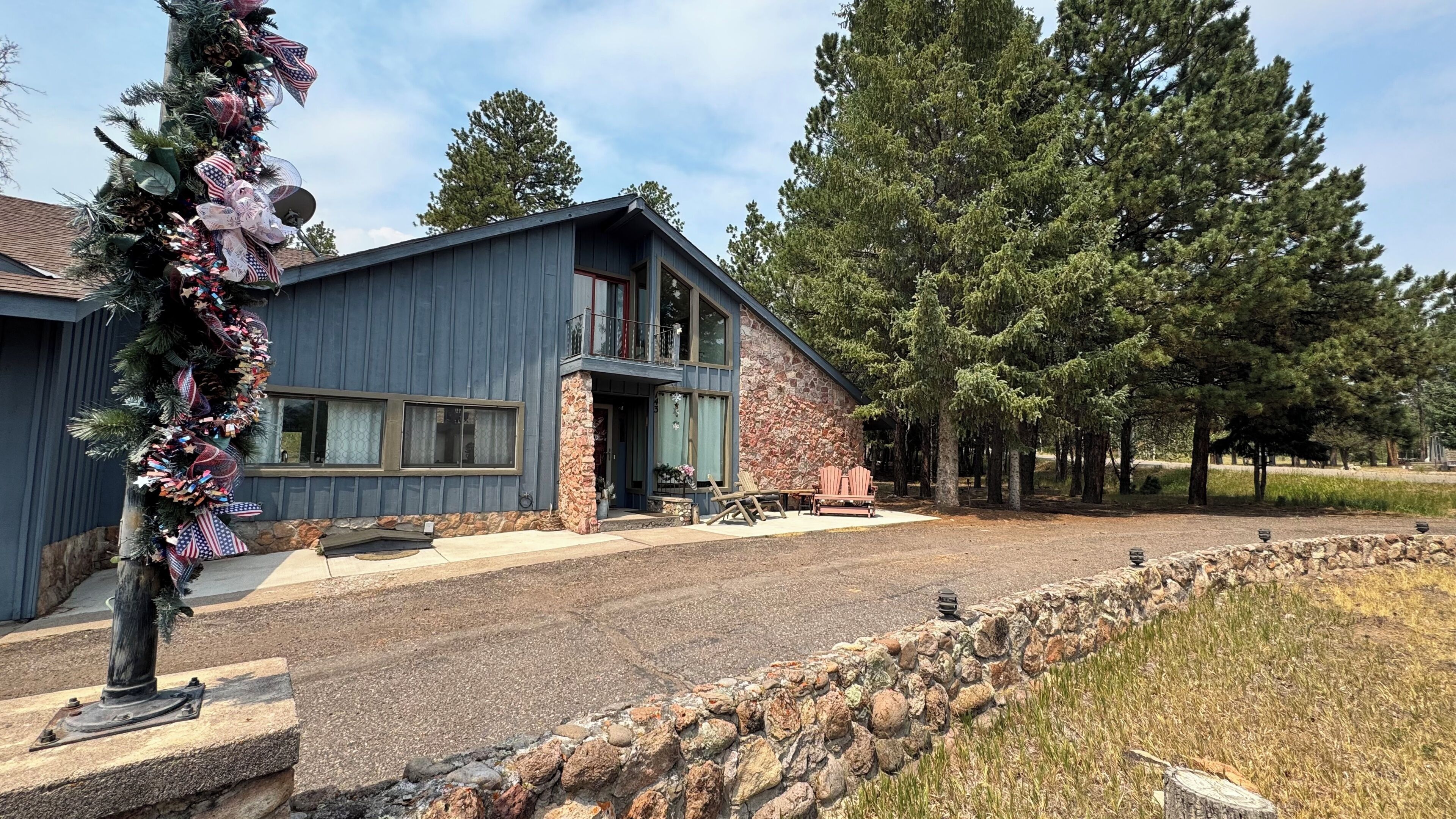 A modern house with a stone facade, large windows, and a stone retaining wall.
