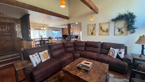 Ein geräumiges Wohnzimmer mit einer großen, winkelförmigen Eckcouch, einem Holztisch und einer Küche im Hintergrund.