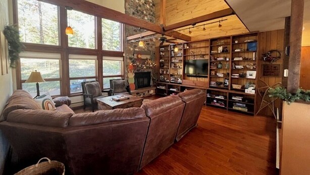 Ein großzügiges Wohnzimmer mit einer großen Eckcouch, Holzboden, einer Steinwand und einem Fernseher.