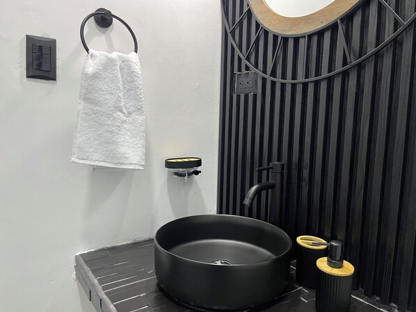 Une salle de bain moderne avec un lavabo noir, une serviette suspendue à un porte-serviette en forme d’anneau et un miroir fixé au mur.