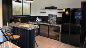 A modern kitchen with a marble countertop, two pendant lights, a refrigerator, and a window with a view of greenery. - Villa Luciérnaga: Private Pool and Total Relaxation (Provincia de Alajuela)
