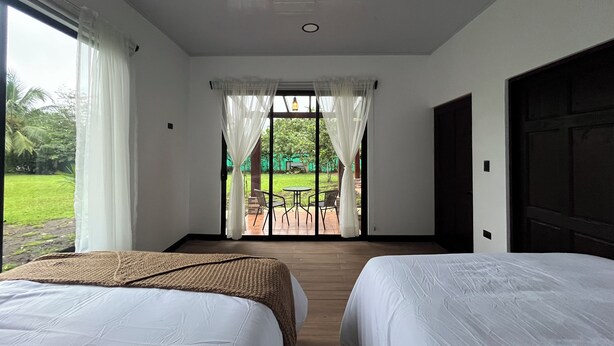 A hotel room with two beds, a view of the garden, and a patio area with chairs. - Villa Luciérnaga: Private Pool and Total Relaxation (Provincia de Alajuela)