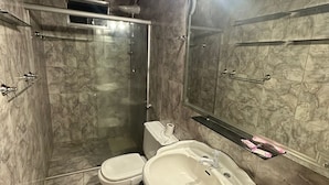 A bathroom with a marble floor, a pedestal sink, a toilet, and a glass-enclosed shower.