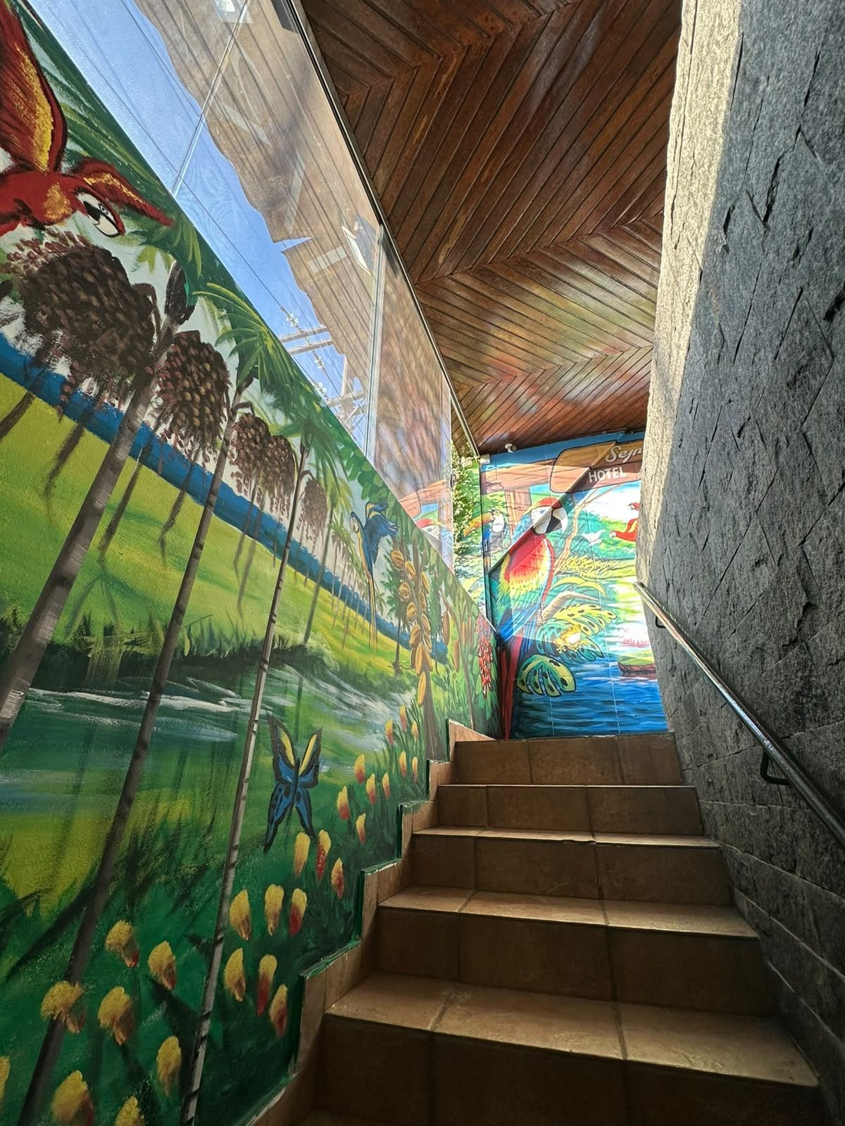 A staircase with a mural on the wall, leading to a room with a wooden ceiling.