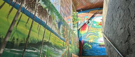 Una escalera con un mural en la pared, que lleva a una habitación con techo de madera.