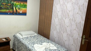 A small, neatly arranged bedroom with a bed, a nightstand, a painting, and an air conditioning unit on the wall.