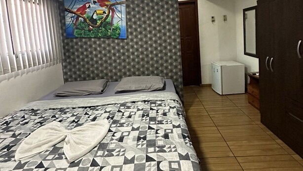 A bedroom with a bed, a painting, a wardrobe, and a small refrigerator.
