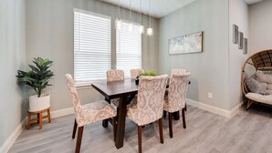 Un comedor con una mesa de madera y sillas estampadas, una planta en maceta y una silla de mimbre.