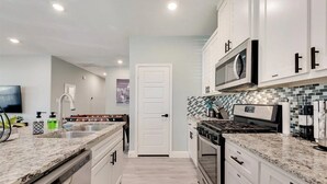 Cocina moderna con armarios blancos, encimera de granito, electrodomésticos de acero inoxidable y salpicadero de azulejos.