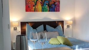 A hotel room with a bed, pillows, a bedside table with a coffee pot and glasses, and a colorful painting above the bed. - Lakeside Heaven. Apartment directly in the Lipno reservoir (Frymburk)