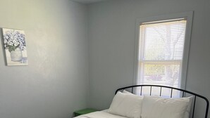 A neatly made bed in a room with a single window and a green nightstand.