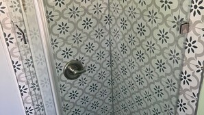 A shower with a glass door and a patterned tile wall.