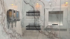 A bathroom with marble walls, a glass shower enclosure, and a black towel rack.