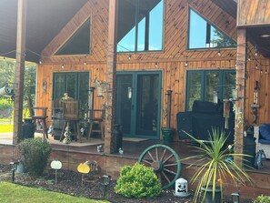 A wooden cabin with large windows, a porch with outdoor seating, and decorative elements like a wagon wheel and lanterns. - ATV/Snow trails! Huge Cov. Patio/A/C, Firepit, Clean, Spacious,Quiet, Att Garage (Crivitz)