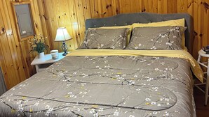 Ein Schlafzimmer mit Holzwand, einem Bett mit floralem Bettzeug, einem Nachttisch mit Lampe und einem Schild über dem Bett.